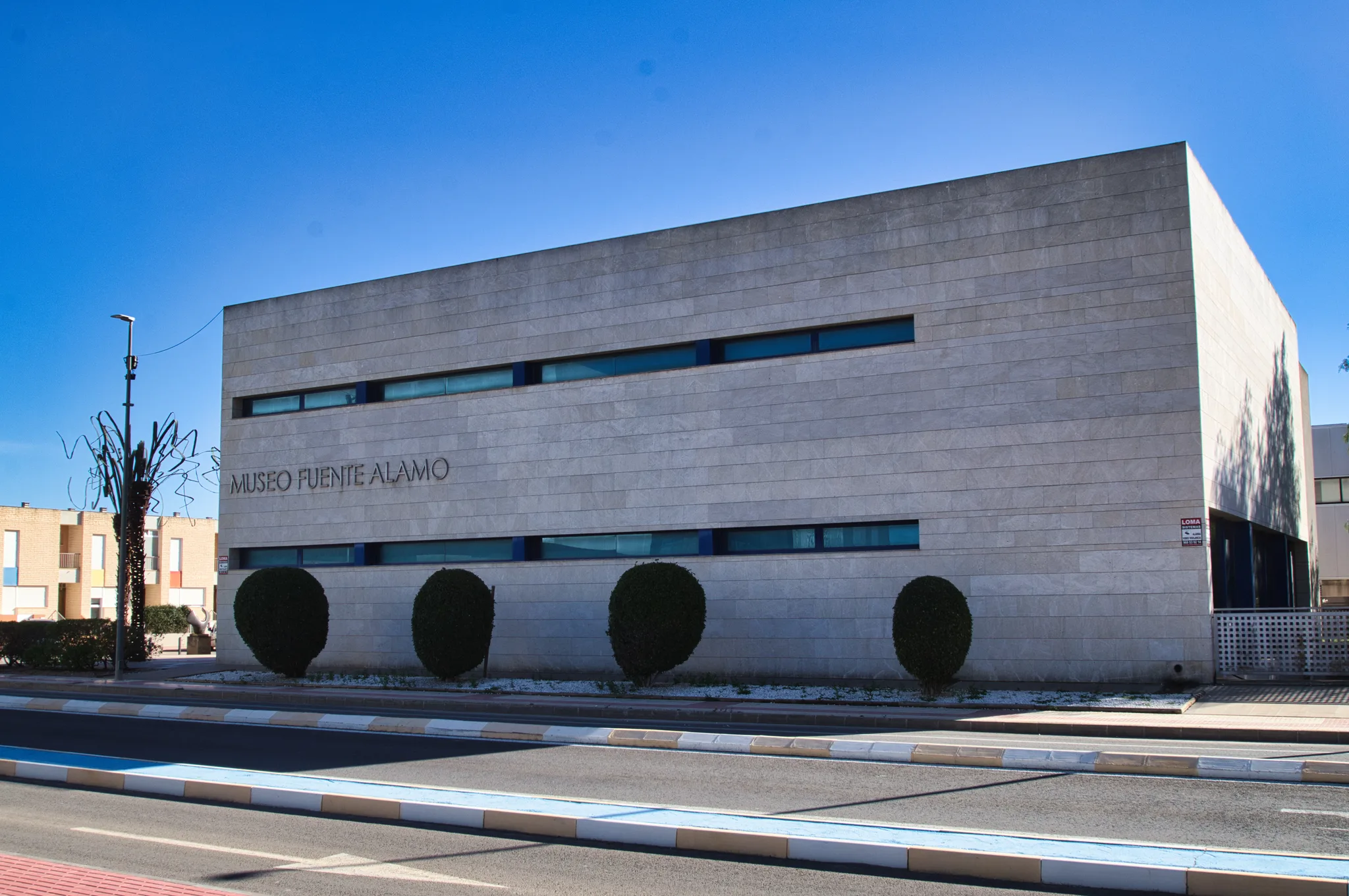 Exterior de piedra moderno del Museo de Fuente Álamo bajo un cielo azul claro