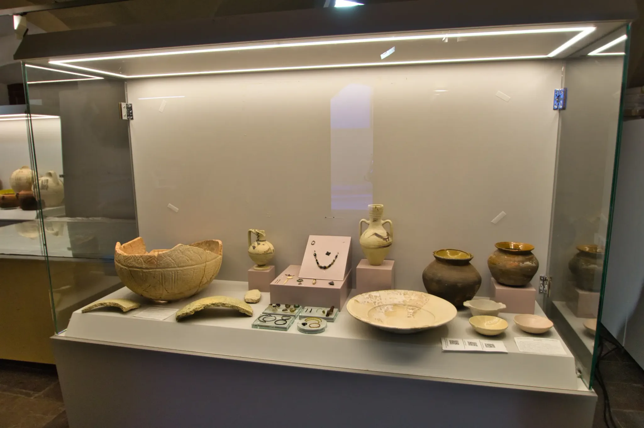 Historic ceramic vessels, bowls and small finds arranged in a glass display case