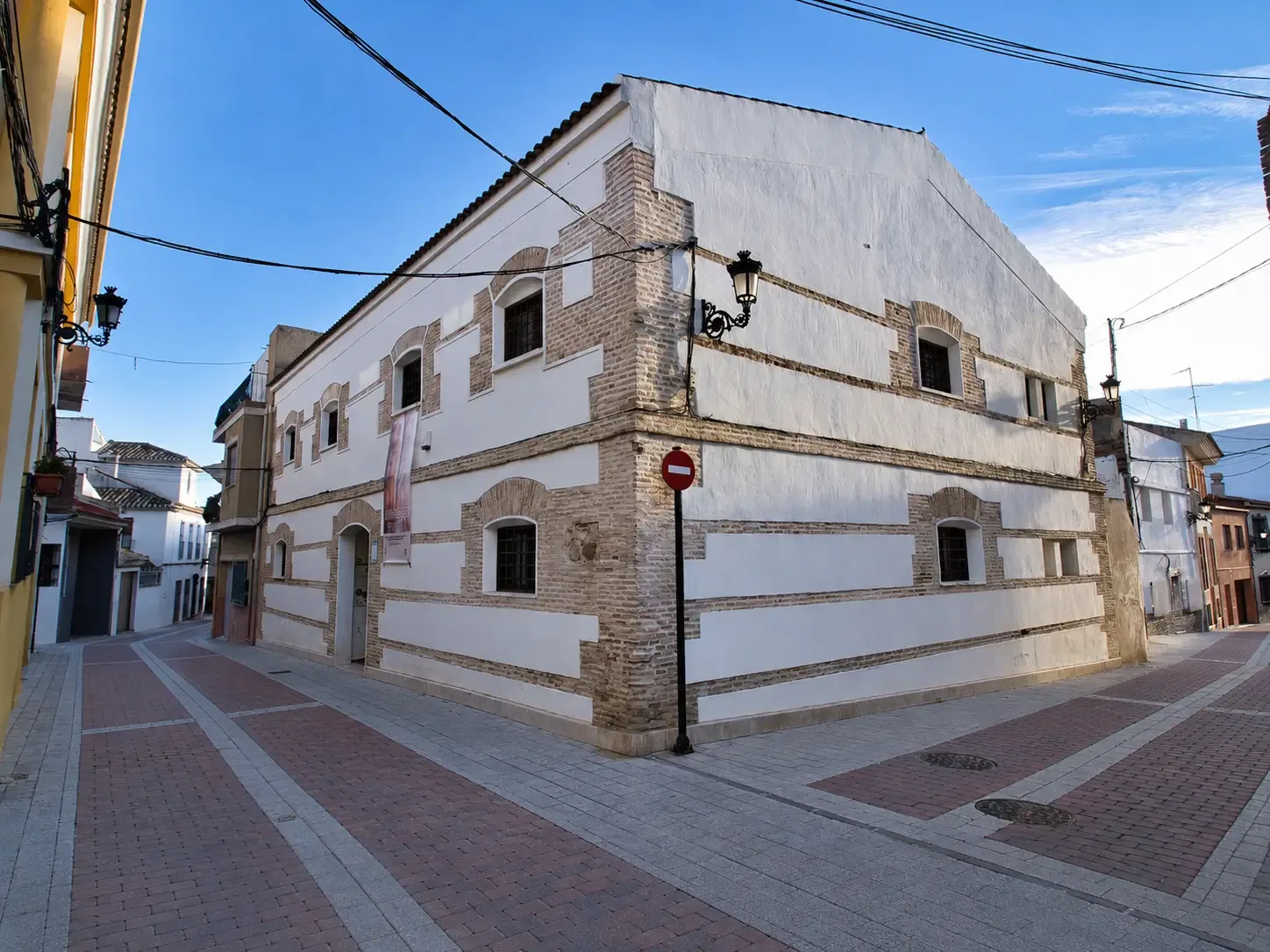 Whitewashed brick-and-masonry exterior of El Pósito Municipal on a narrow street in Alhama de Murcia
