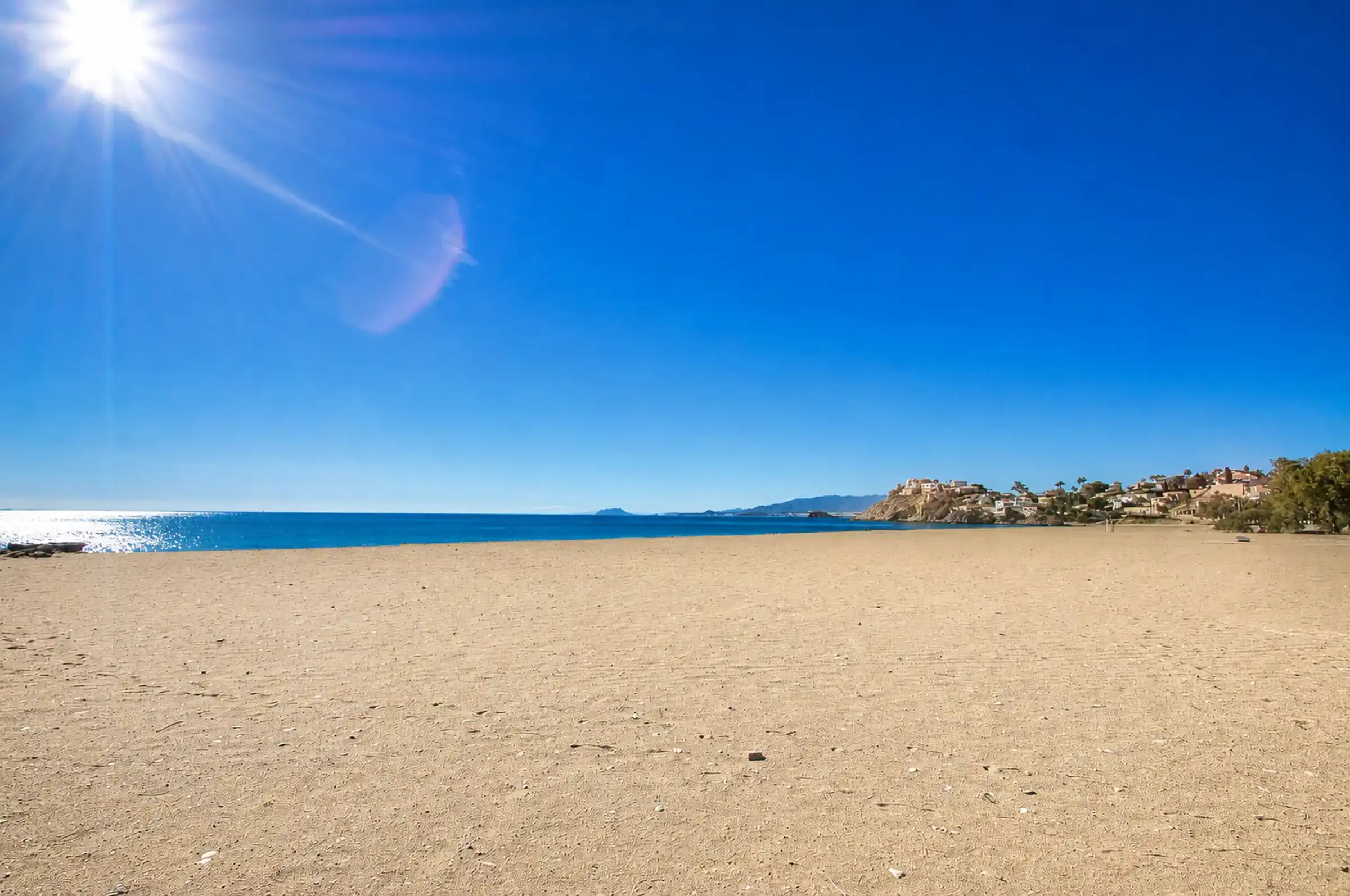 A sandy Mediterranean beach beneath a clear blue sky in the Region of Murcia