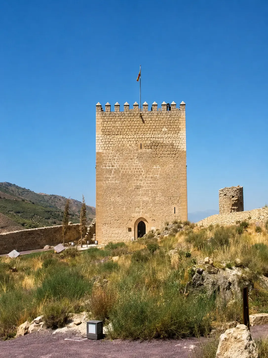 Square crenellated stone tower with a Spanish flag inside Lorca Castle