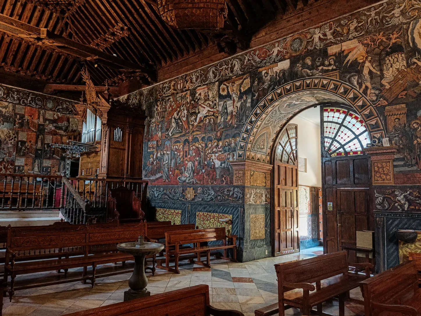 Painted wall, arched doorway and wooden seating inside Santa Eulalia Sanctuary