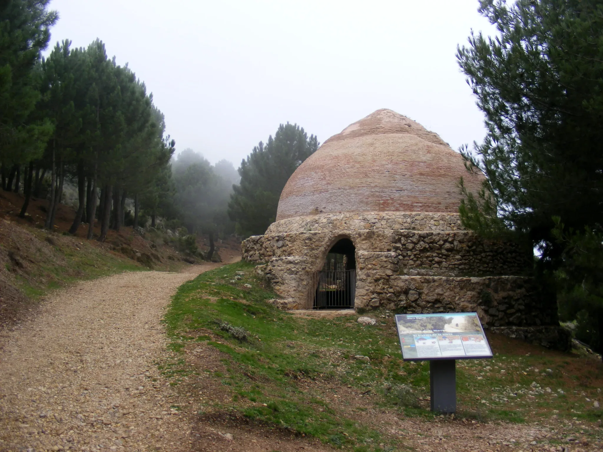 Pozo de nieve histórico abovedado junto a un camino entre pinos y niebla en Sierra Espuña